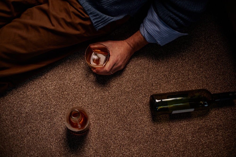 individual sitting on the floor with glass half empty of alcohol
