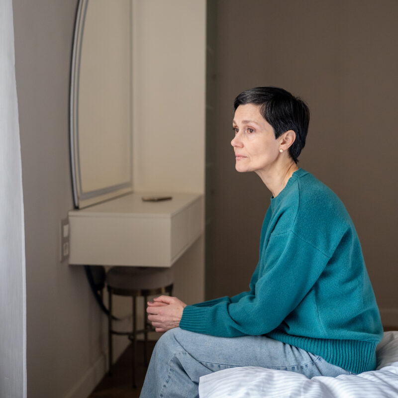 A woman sitting on a bed wondering how long is an inpatient mental health stay.