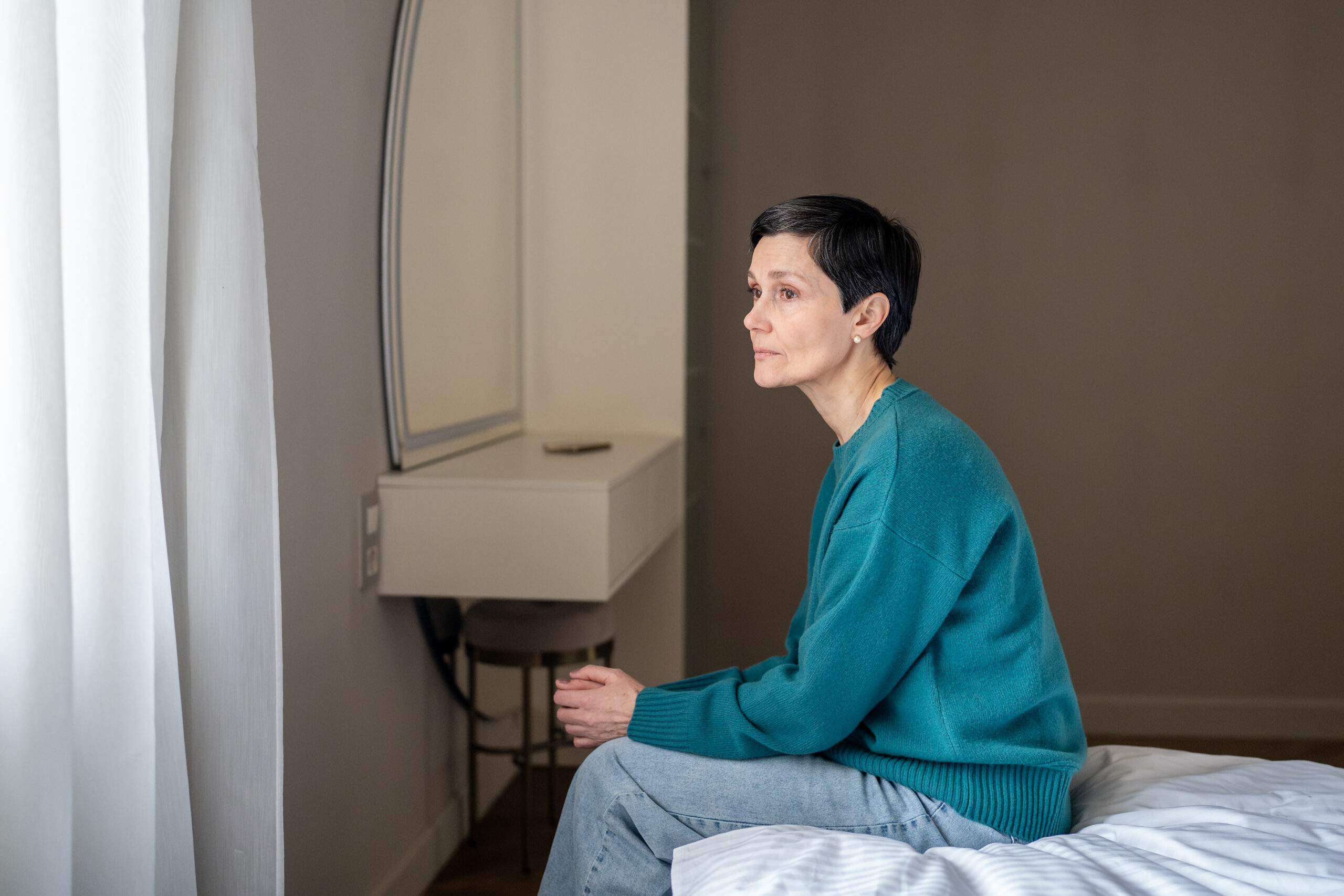 A woman sitting on a bed wondering how long is an inpatient mental health stay.